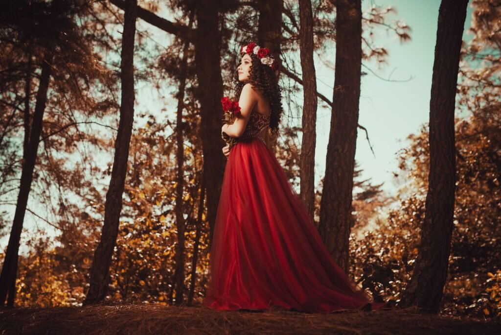 Woman in a flowing red dress and floral crown standing in a forest, evoking Persephone from Greek myth