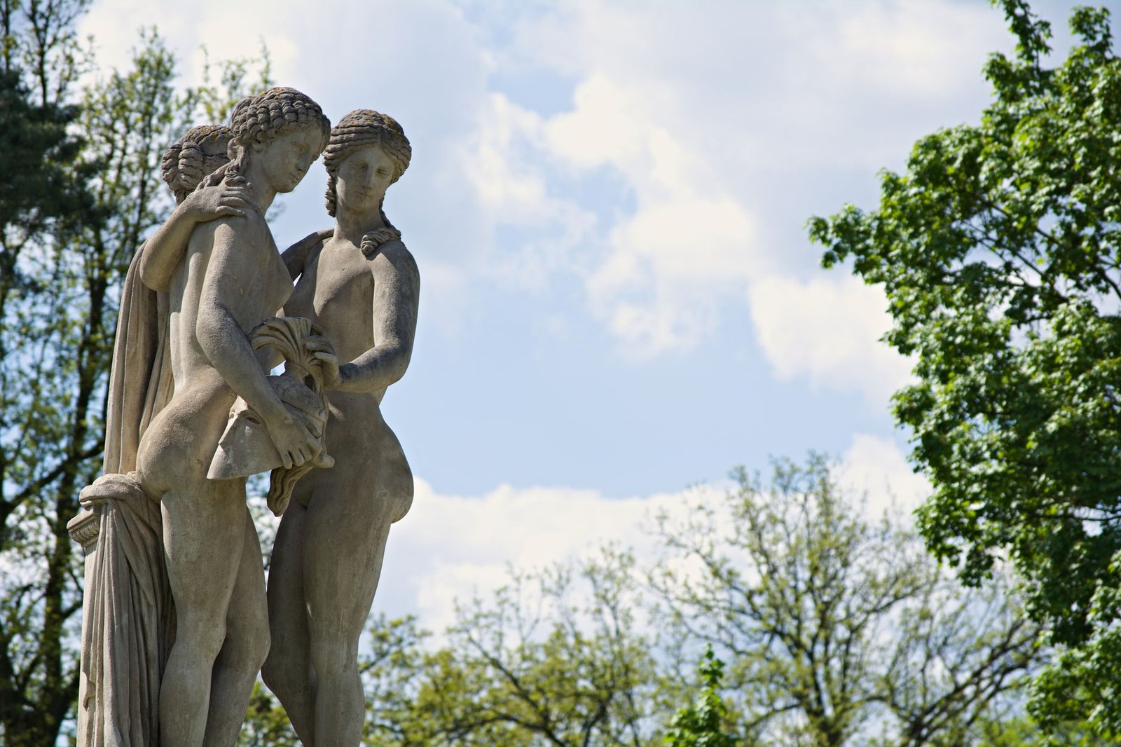 Classical stone statue of Adonis and Aphrodite in a lush garden with trees and foliage