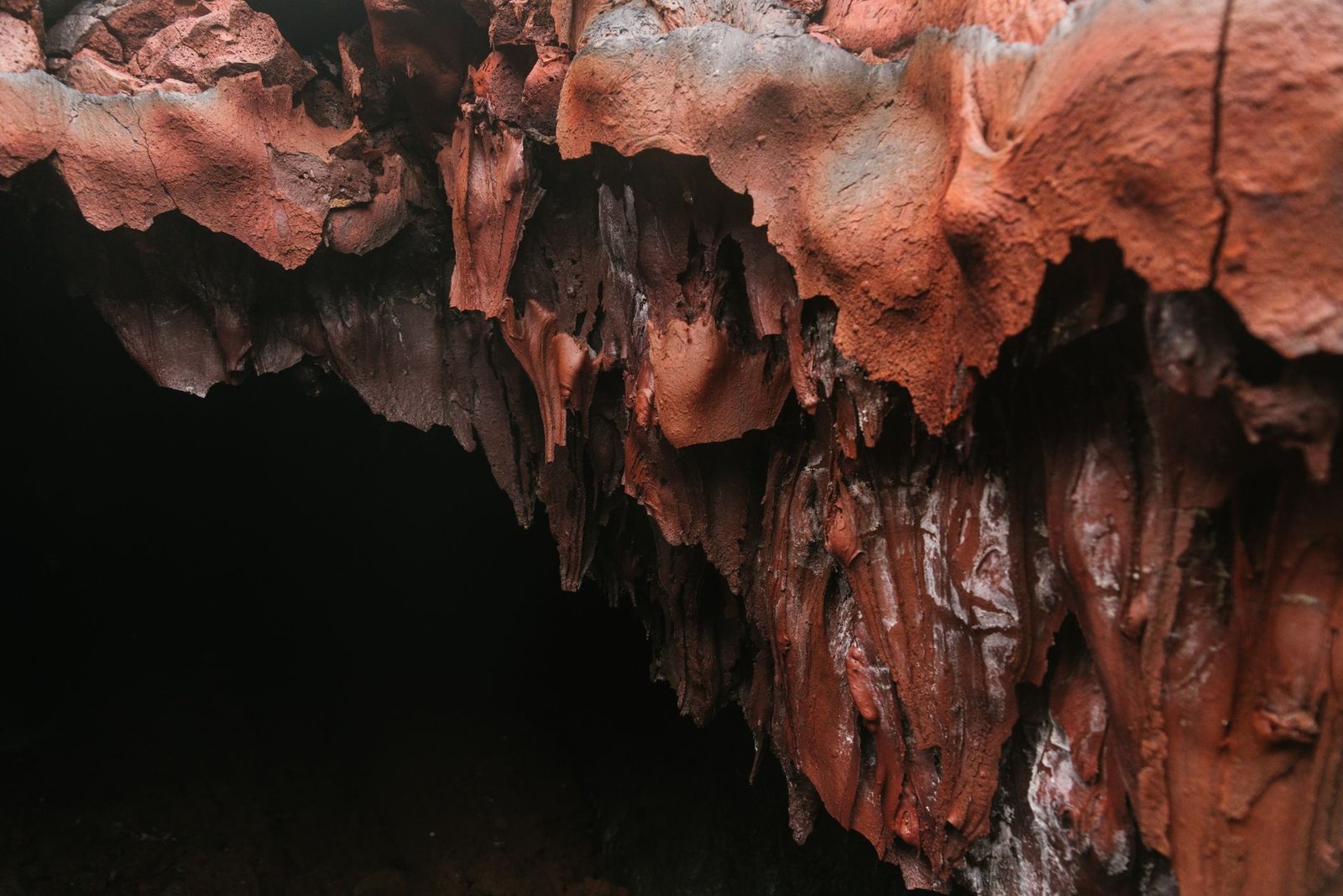 Red and brown stalactites hang from the ceiling of a dark cave, evoking Aeneas’s descent into the underworld