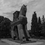 Black and white photo of a wooden Trojan horse statue in a park, representing the myth of Aeneas's flight from Troy