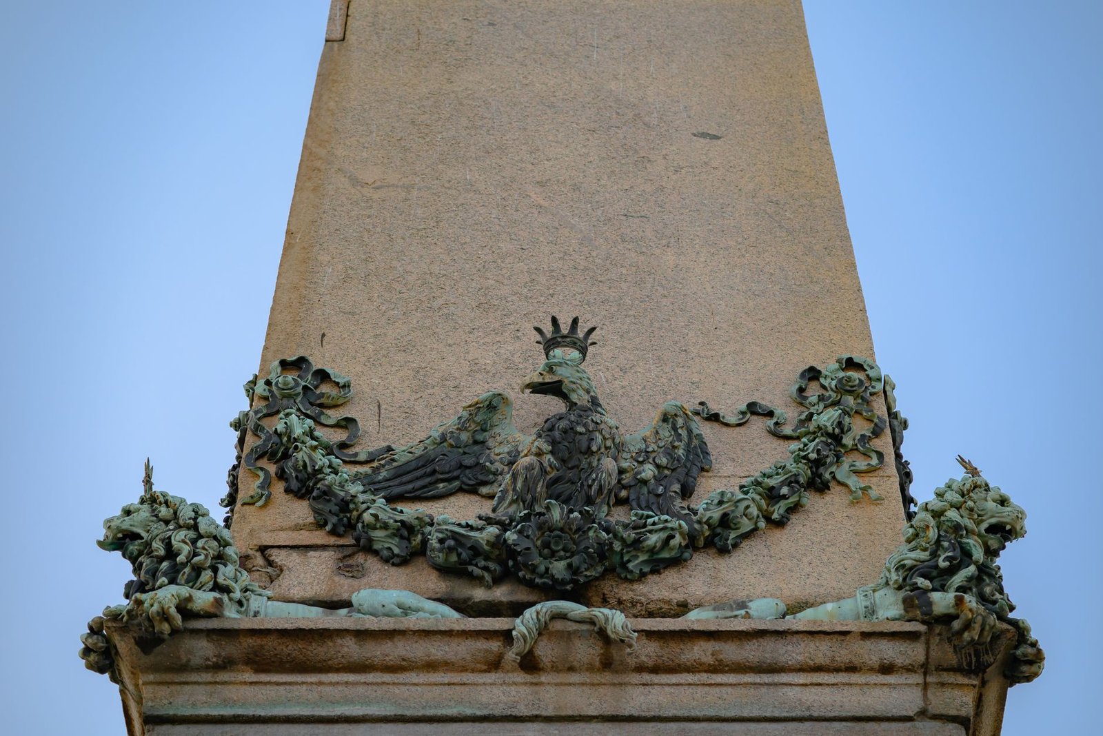 Bronze eagle sculpture atop a stone monument against a clear blue sky