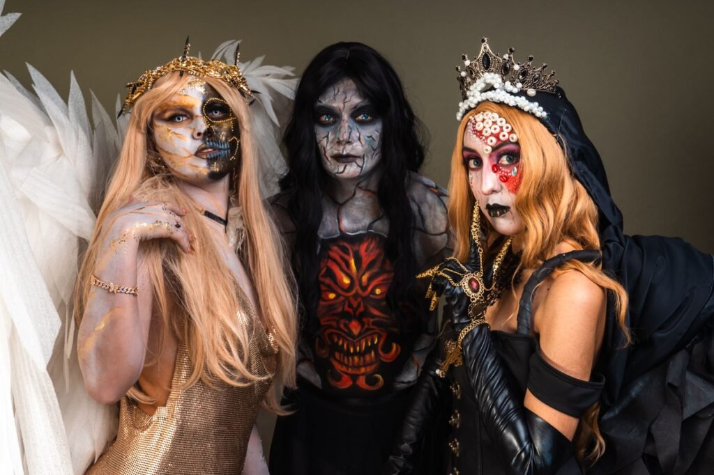 Three people in elaborate Halloween costumes and makeup posing against a plain background