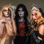 Three people in elaborate Halloween costumes and makeup posing against a plain background