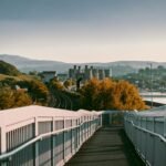 Pedestrian bridge leading to a cityscape with hills and water in the background, evoking Welsh inspiration and Awen