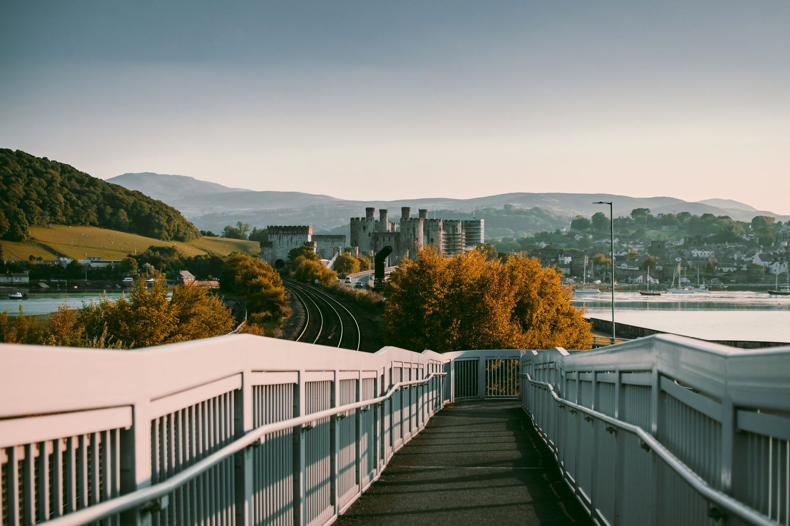 Pedestrian bridge leading to a cityscape with hills and water in the background, evoking Welsh inspiration and Awen