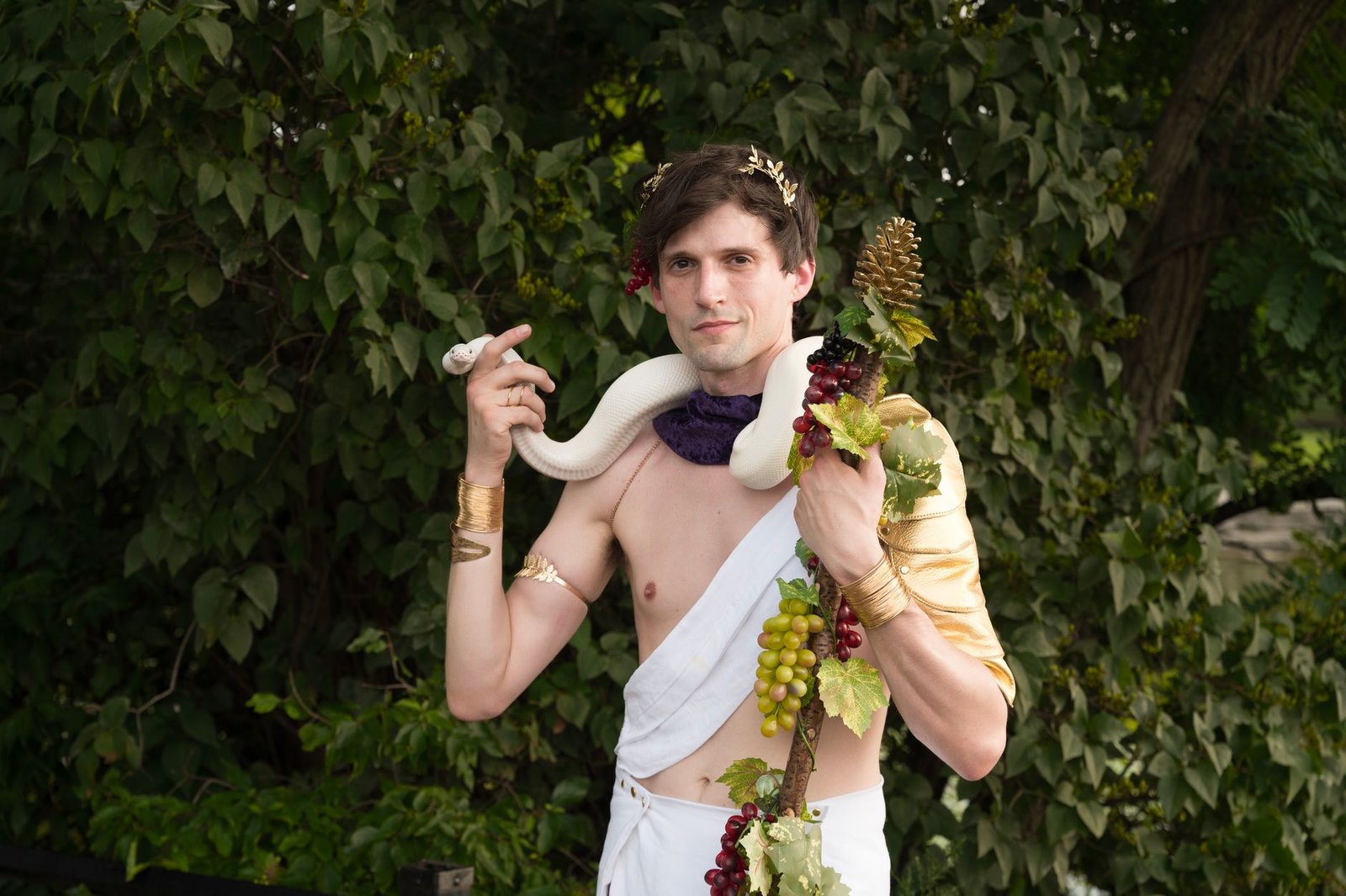 Young man dressed as Bacchus holding grapes and a drinking horn in a natural outdoor setting