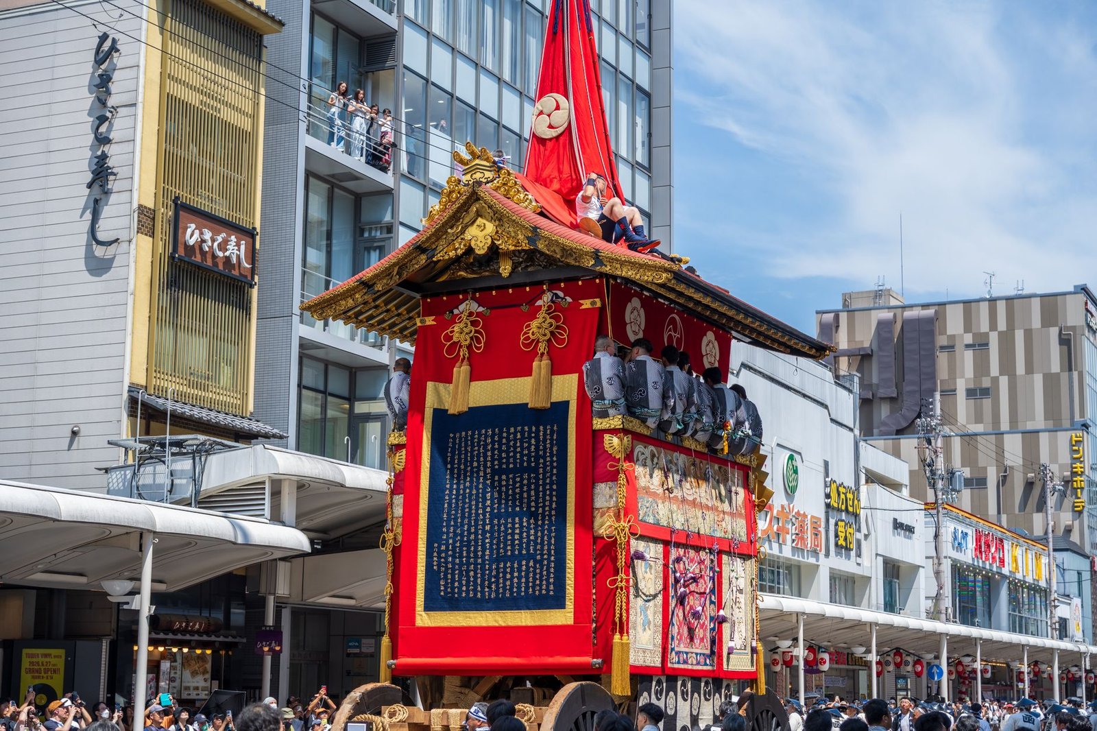 Traditional Japanese festival float parade in a city street, with a Bishamonten statue on the decorated float