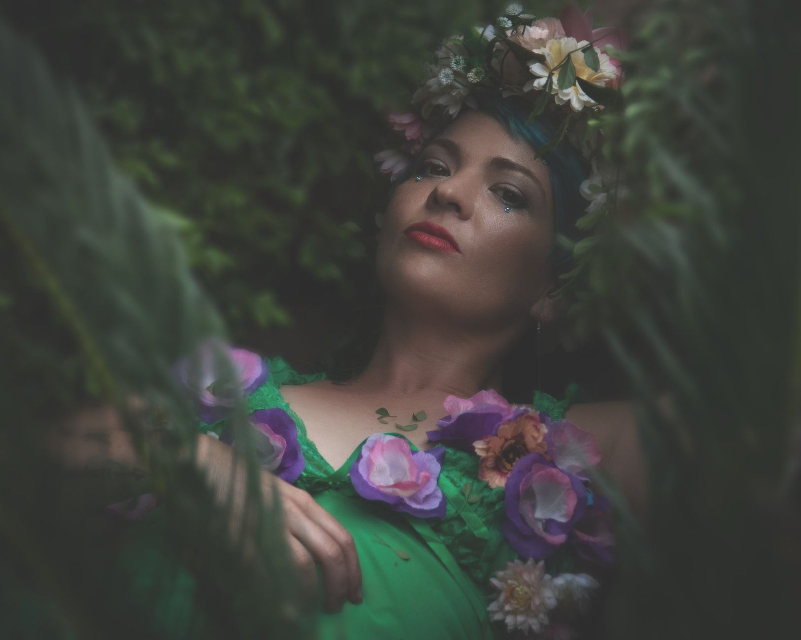 Portrait of a woman in a floral crown and green dress surrounded by lush greenery, evoking Blodeuwedd from Welsh myth
