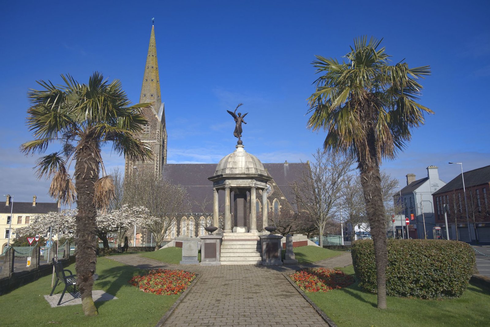 Historic church and monument in a quaint town square, surrounded by palm trees, evoking Branwen and the War with Ireland