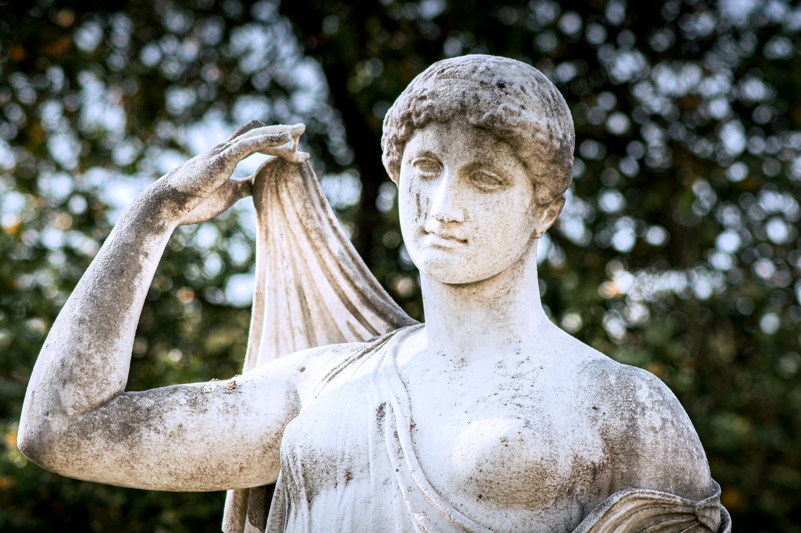 Ancient marble statue of a woman in a draped garment standing in an outdoor garden, representing Branwen from Welsh mythology
