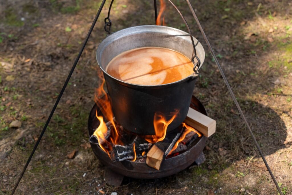 Iron pot suspended over an open campfire, with flames beneath for cooking outdoors.