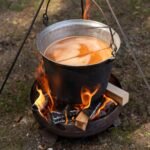Iron pot suspended over an open campfire, with flames beneath for cooking outdoors.
