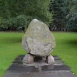Memorial stone monument in a peaceful park surrounded by greenery, honoring Cú Chulainn's Boyhood Deeds