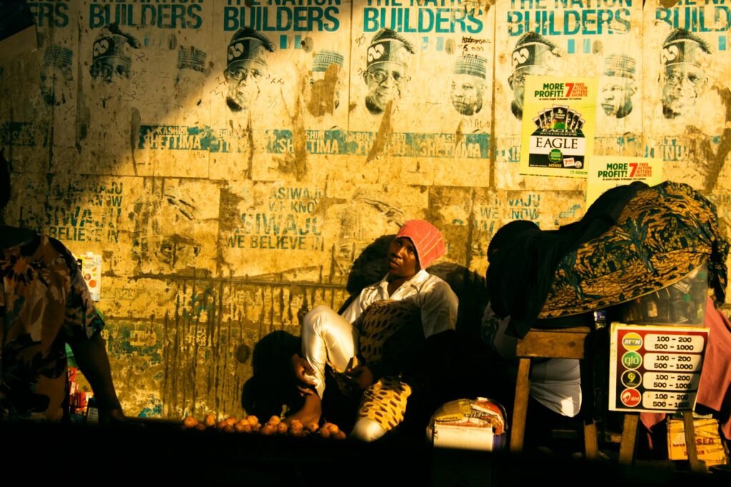 Night street vendor selling goods beside a poster-covered wall with a hound motif suggesting Cwn Annwn