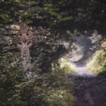 Ancient Celtic cross on a forest path surrounded by dense green foliage and misty woodland scenery