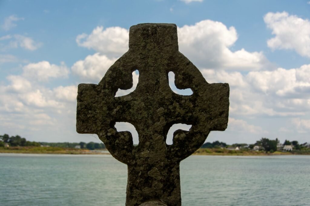 Ancient Celtic cross monument overlooking a serene lake under a partly cloudy sky