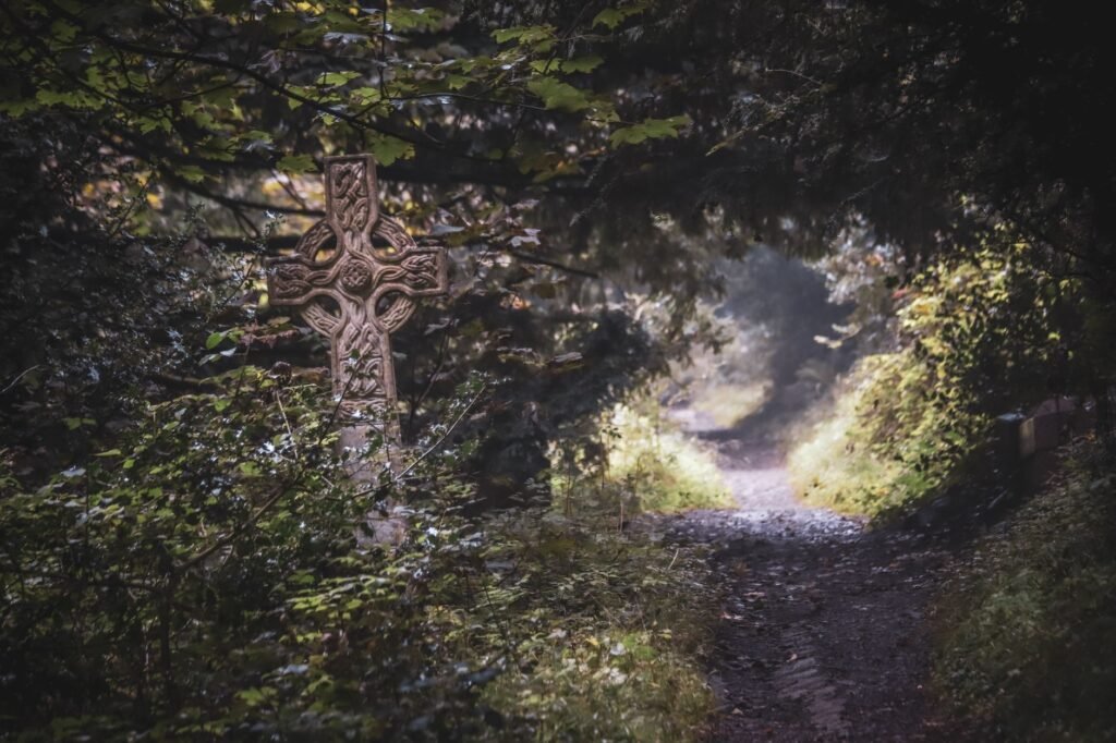 Ancient Celtic cross on a forest path surrounded by dense greenery and mist