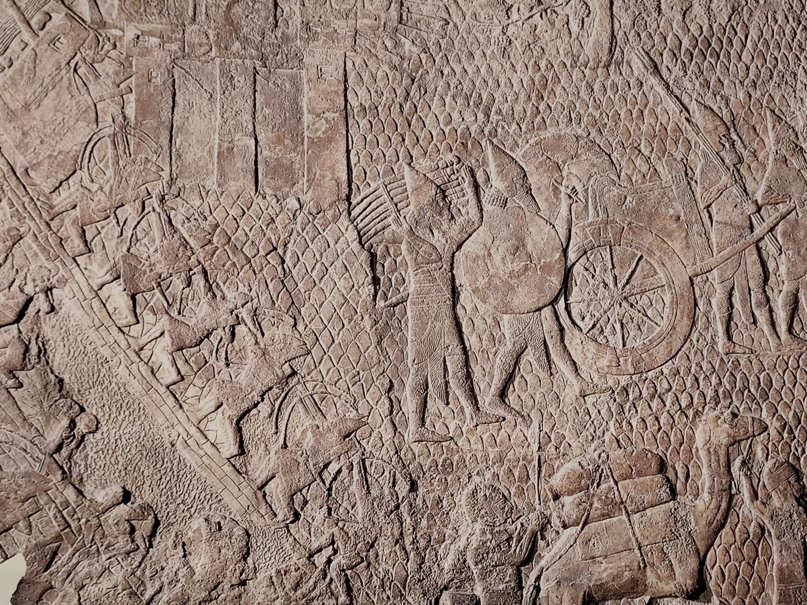Ancient Assyrian stone relief of a battle scene with soldiers, chariots, and animals, evoking Helios's sun chariot