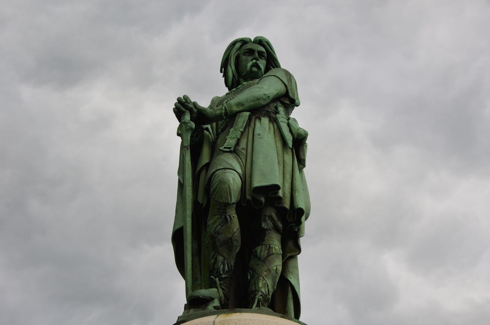 Statue of a historical figure holding a sword against a cloudy sky, representing the chief god in Celtic mythology