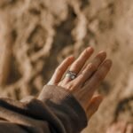 Close-up of a hand wearing a Claddagh ring against a blurred natural background