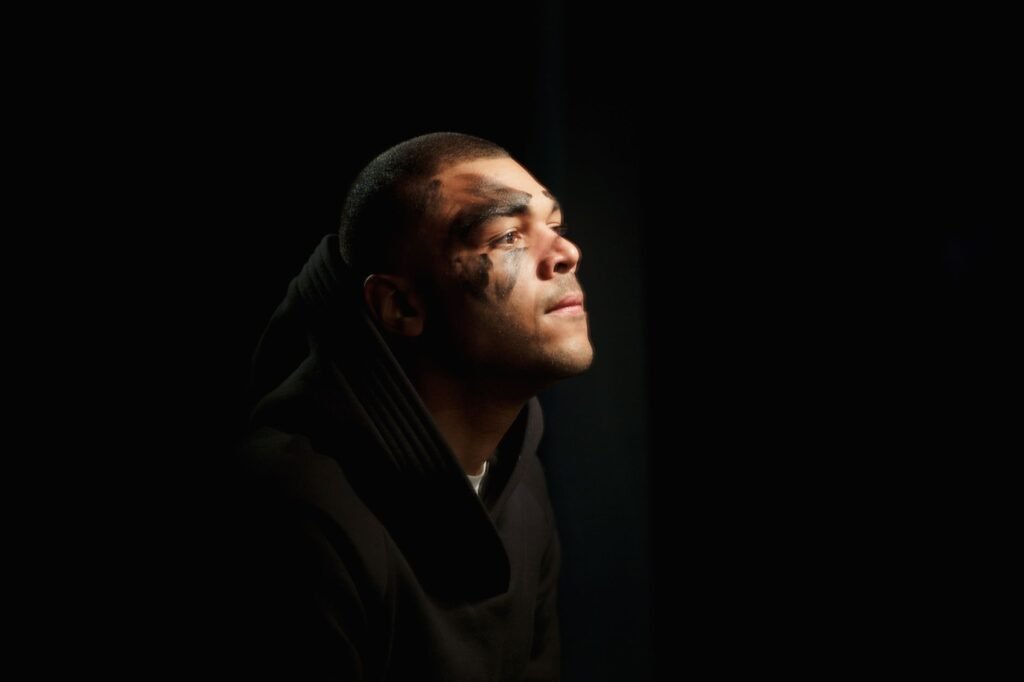Portrait of a person with face paint lit softly against a dark background, evoking Coriolanus’s betrayal and return