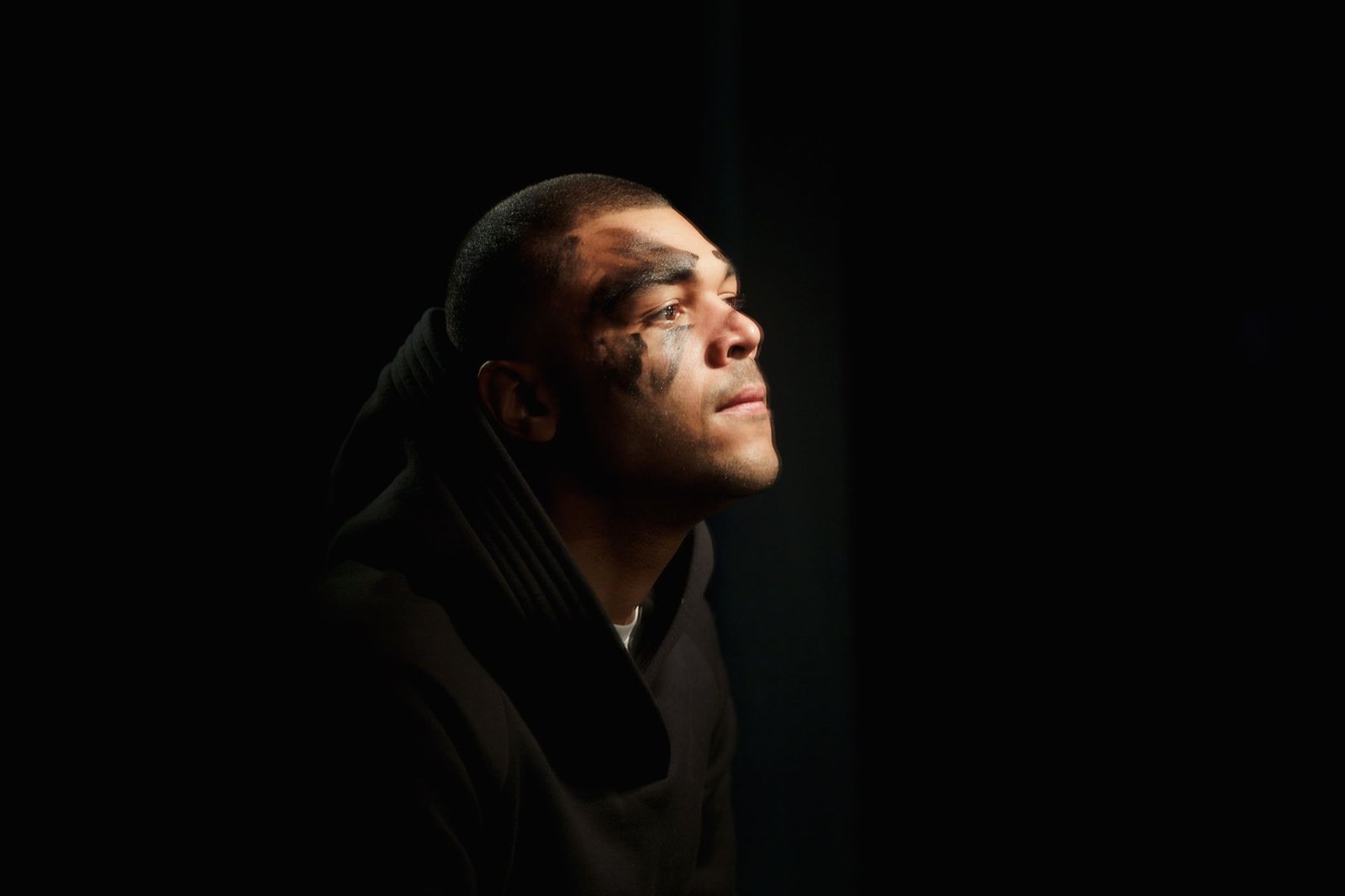 Portrait of a person with face paint lit softly against a dark background, evoking Coriolanus’s betrayal and return