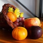 Cornucopia overflowing with oranges, grapes, an apple, plum, and a gourd on a wooden table.