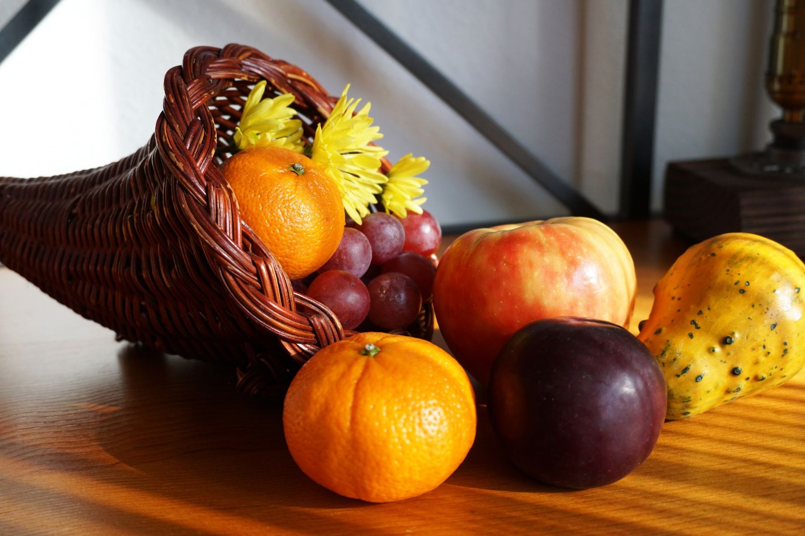 Cornucopia overflowing with oranges, grapes, an apple, plum, and a gourd on a wooden table.