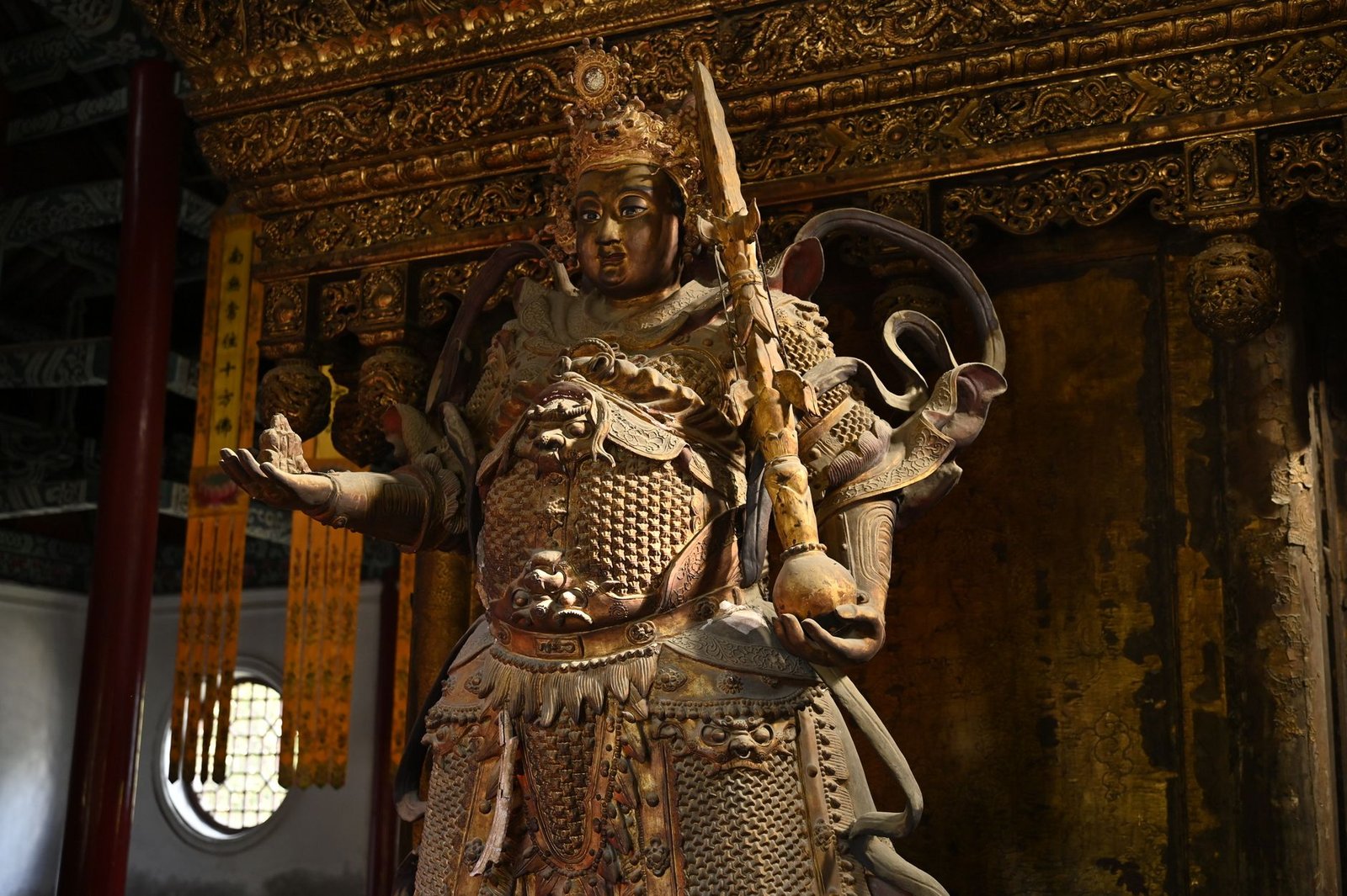 Ancient warrior statue in a traditional temple, representing Daikokuten deity with detailed armor and solemn expression