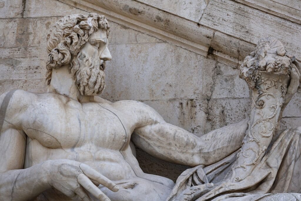 Close-up of a bearded reclining stone sculpture of a Roman god, showing detailed ancient carving and weathered surface