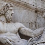 Close-up of an ancient stone sculpture of a reclining bearded Roman god with detailed carved features