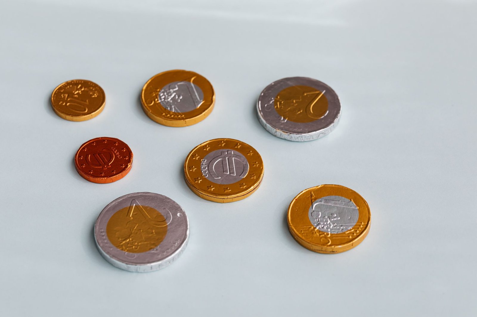 Chocolate coins wrapped in gold and silver foil on a white surface, resembling Roman offerings to household gods