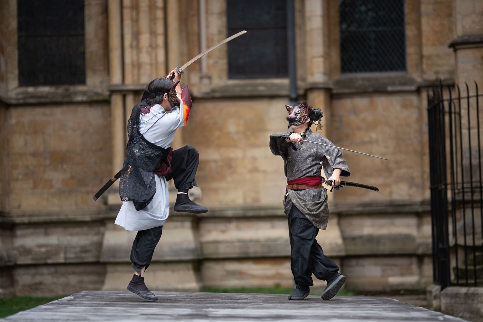 Two martial artists spar with swords outdoors in a traditional duel under open sky