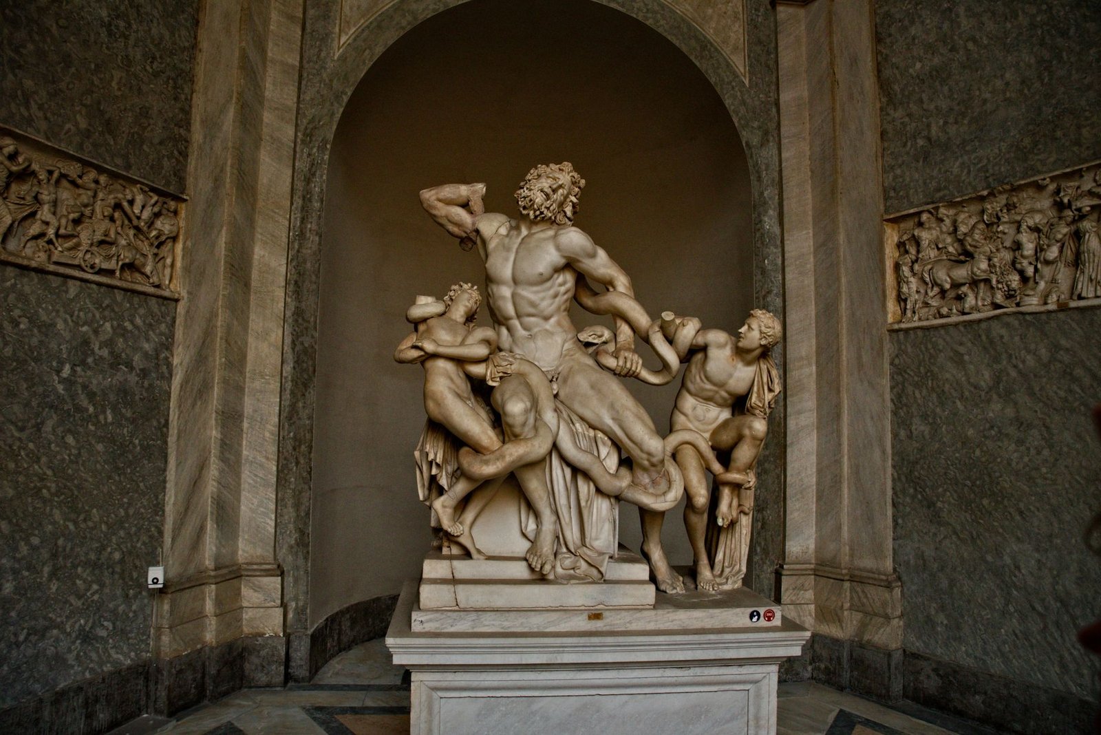Marble statue of Laocoön and his sons in a museum niche, showing the mythological struggle with serpents