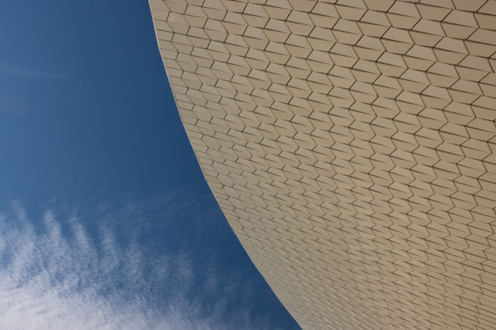 Curved modern building with hexagonal tile pattern against a blue sky, evoking Ma'at's feather in Egyptian mythology