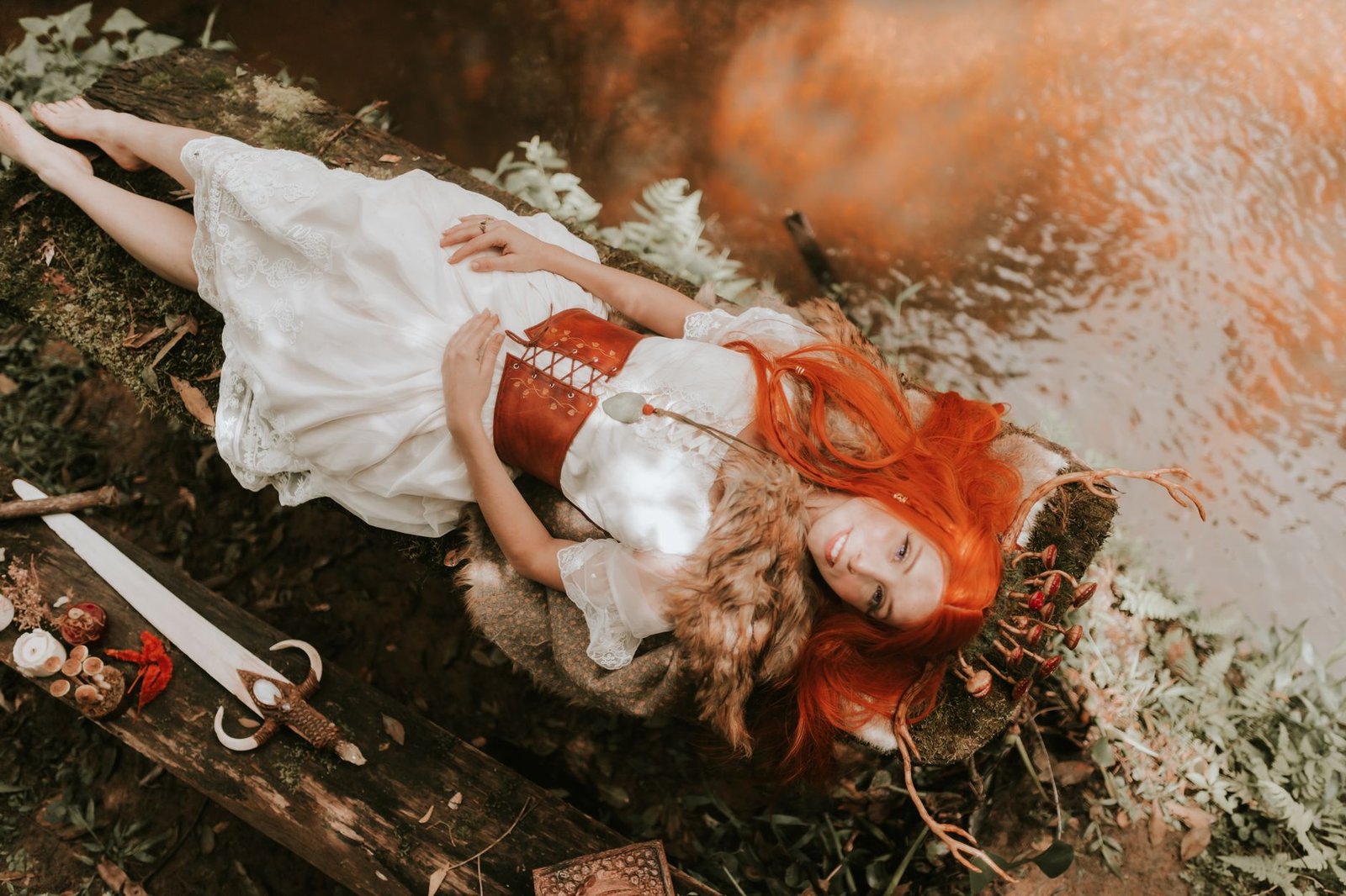 Red-haired woman in medieval dress lying beside a forest stream, evoking Flidais from Irish mythology