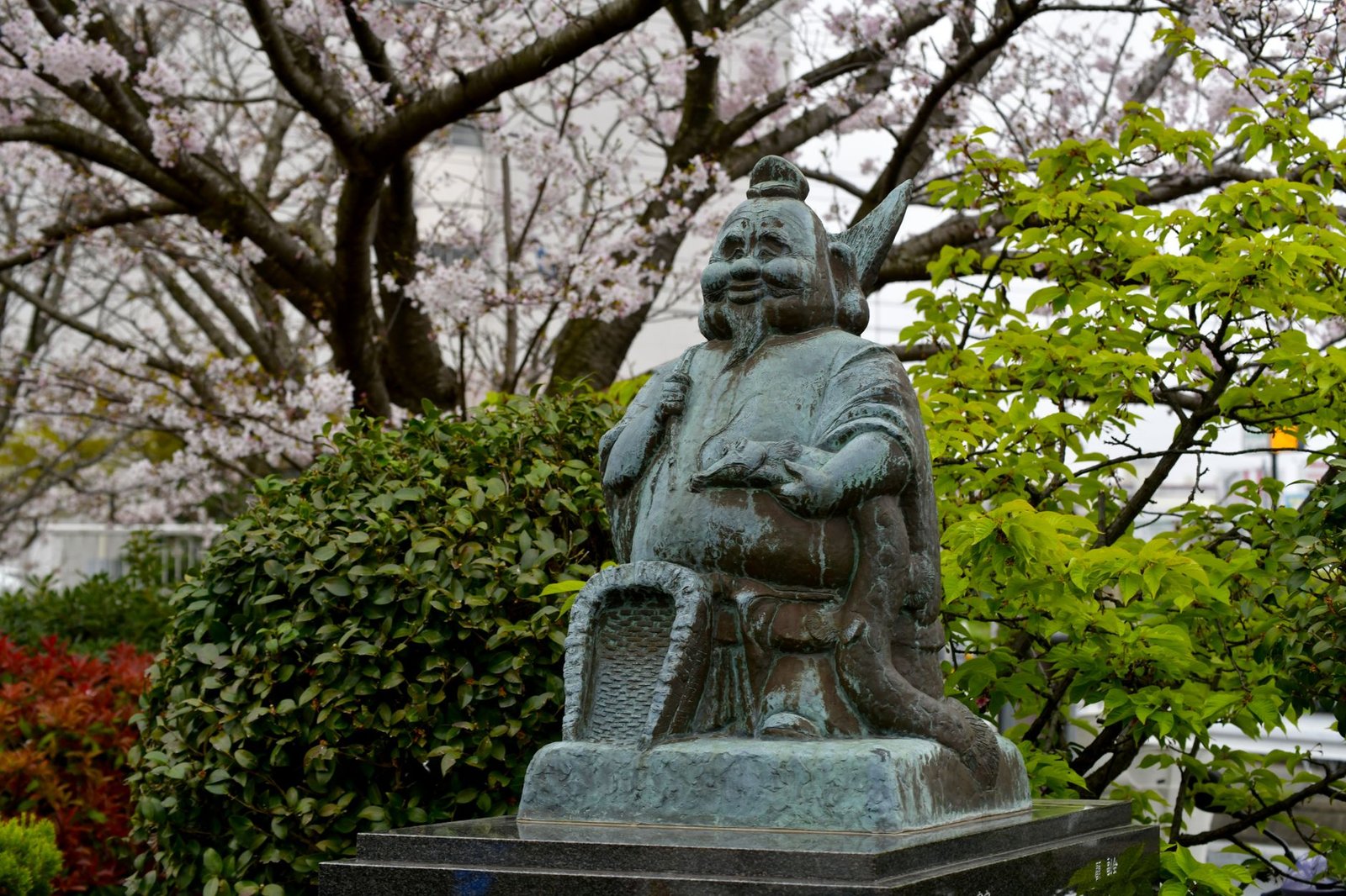 Bronze samurai statue amid lush greenery and cherry blossom trees
