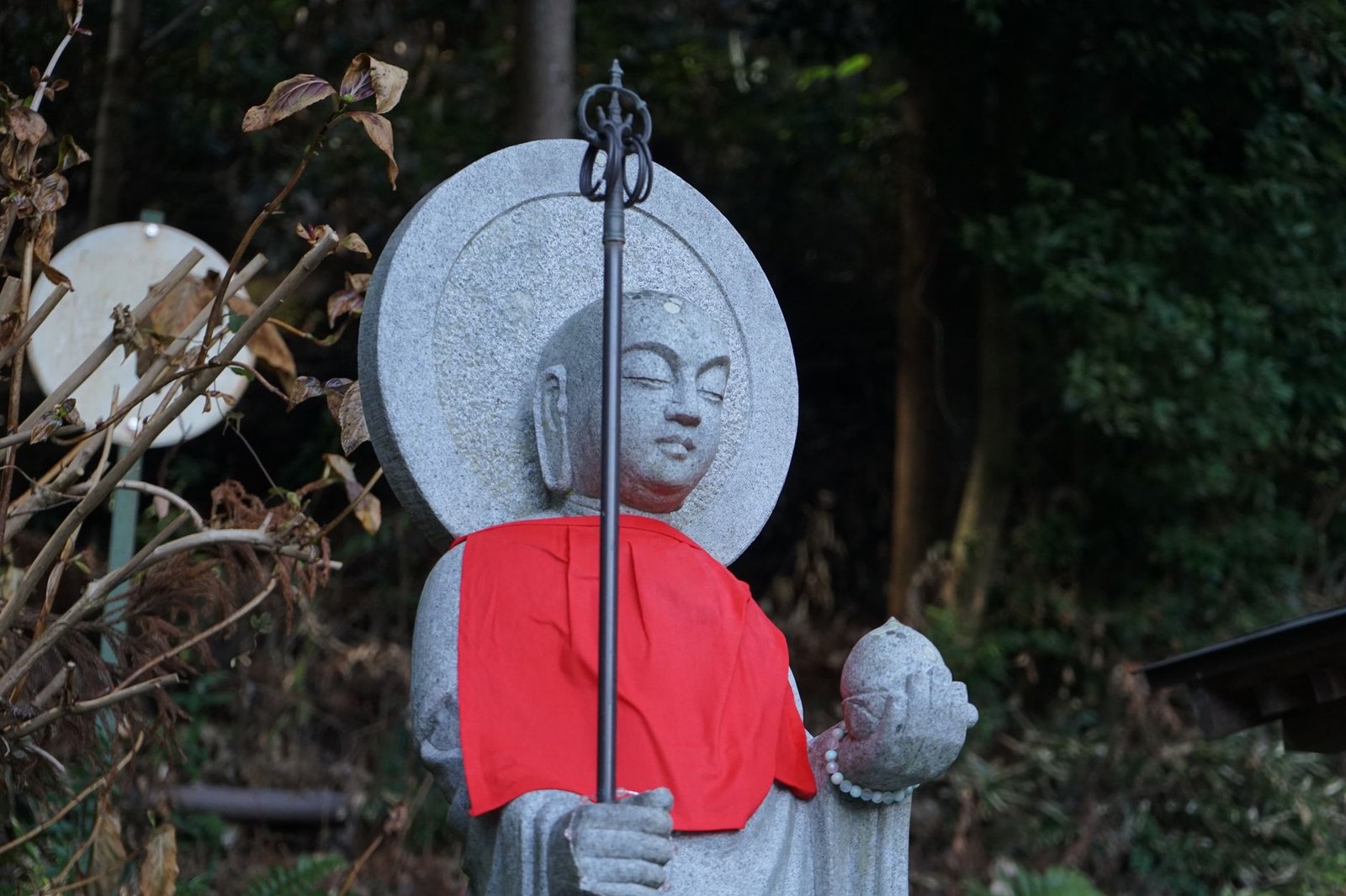 Stone statue of a Buddha-like figure draped in red cloth among trees in a forest setting