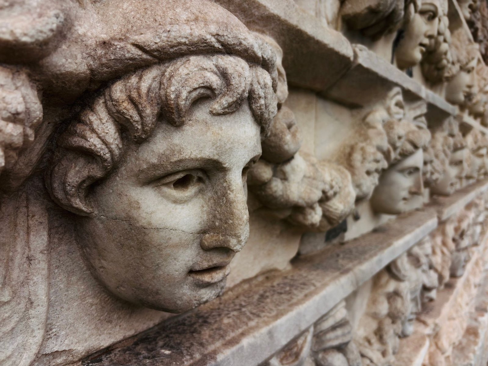 Close-up of ancient stone carved faces on a historic wall, evoking the Greek Furies in Roman mythology