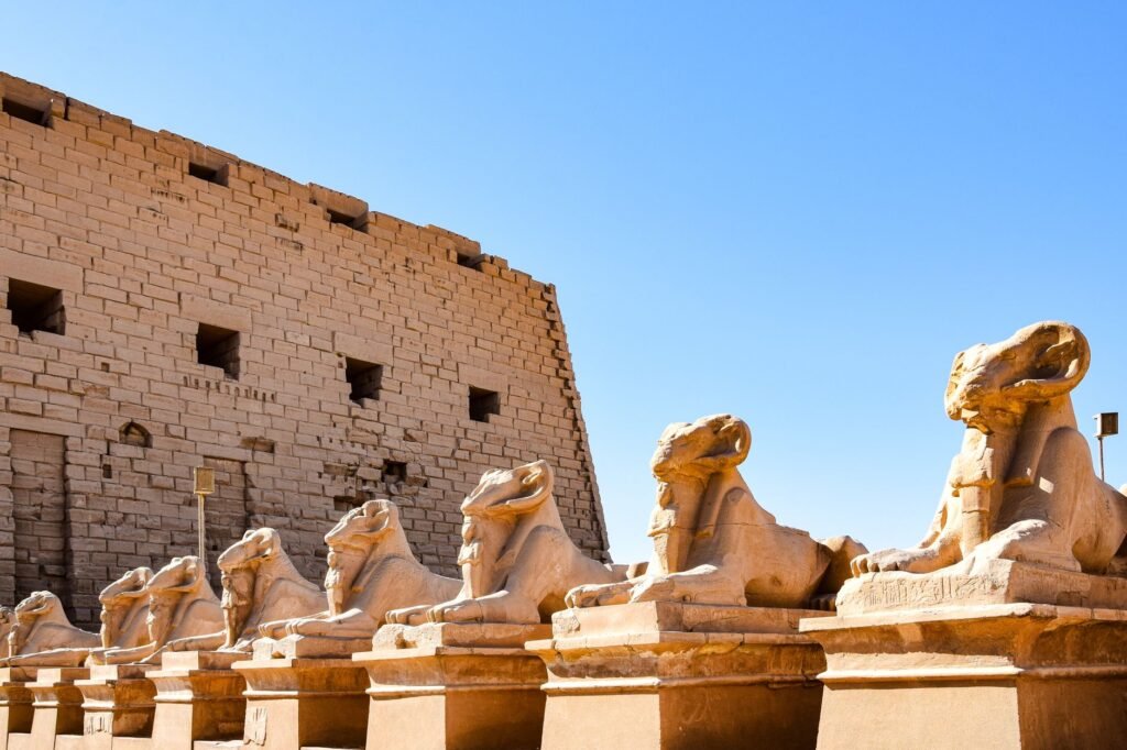 Ancient Egyptian sphinx statues lined up near a historic temple under a clear blue sky