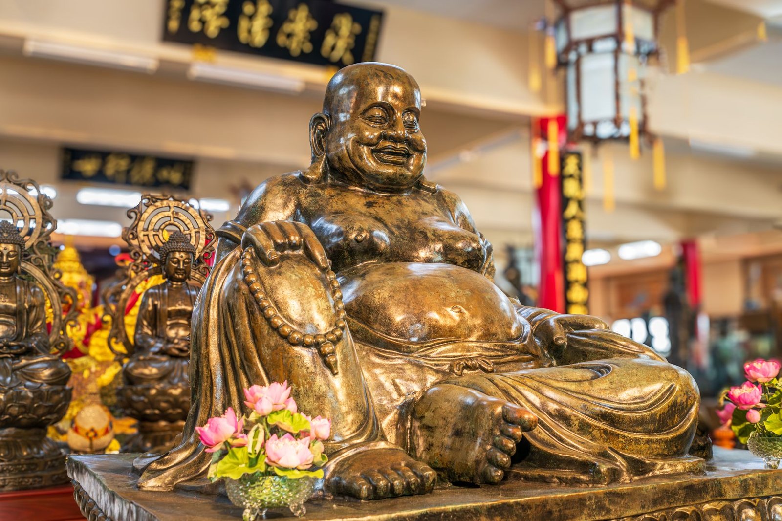 Bronze statue of Hotei, the laughing Buddha, in a traditional Asian temple setting