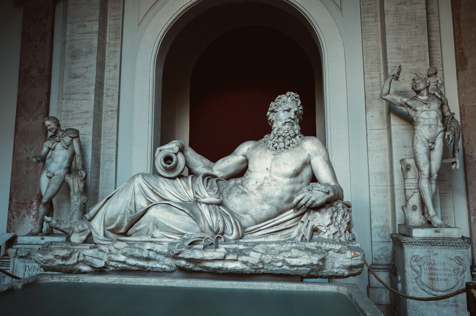 Reclining marble statue of a bearded figure, representing the many gods in Greek mythology in a museum setting