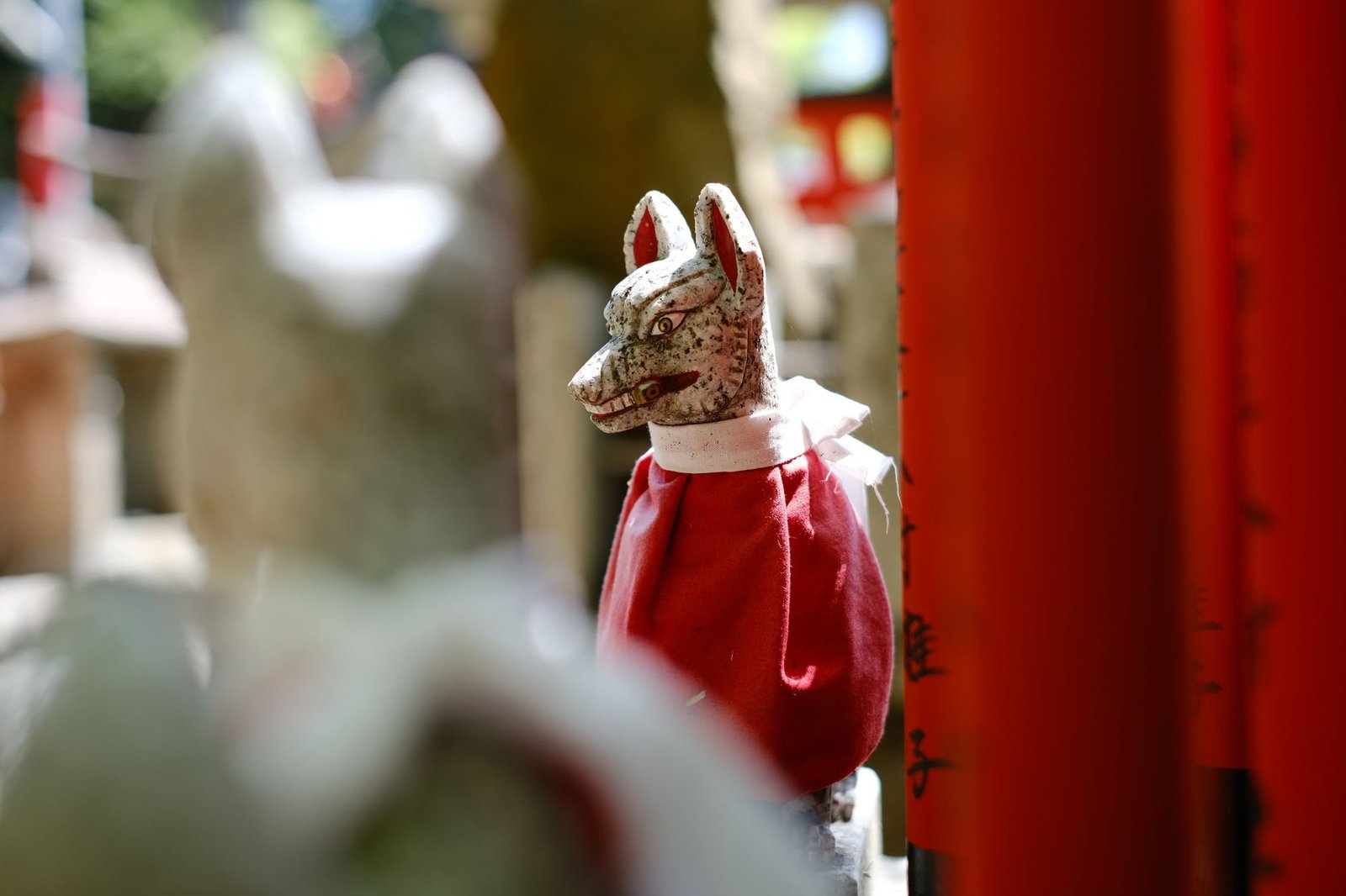 Traditional Japanese fox statue wearing a red bib at a Shinto shrine, representing the Inari deity