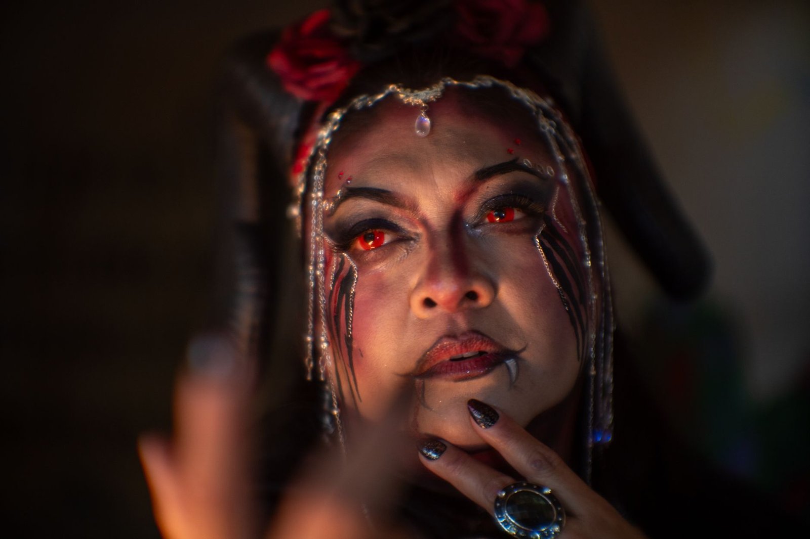 Close-up portrait of a woman with dramatic red eye makeup and an ornate headpiece in low light, evoking an incubus demon