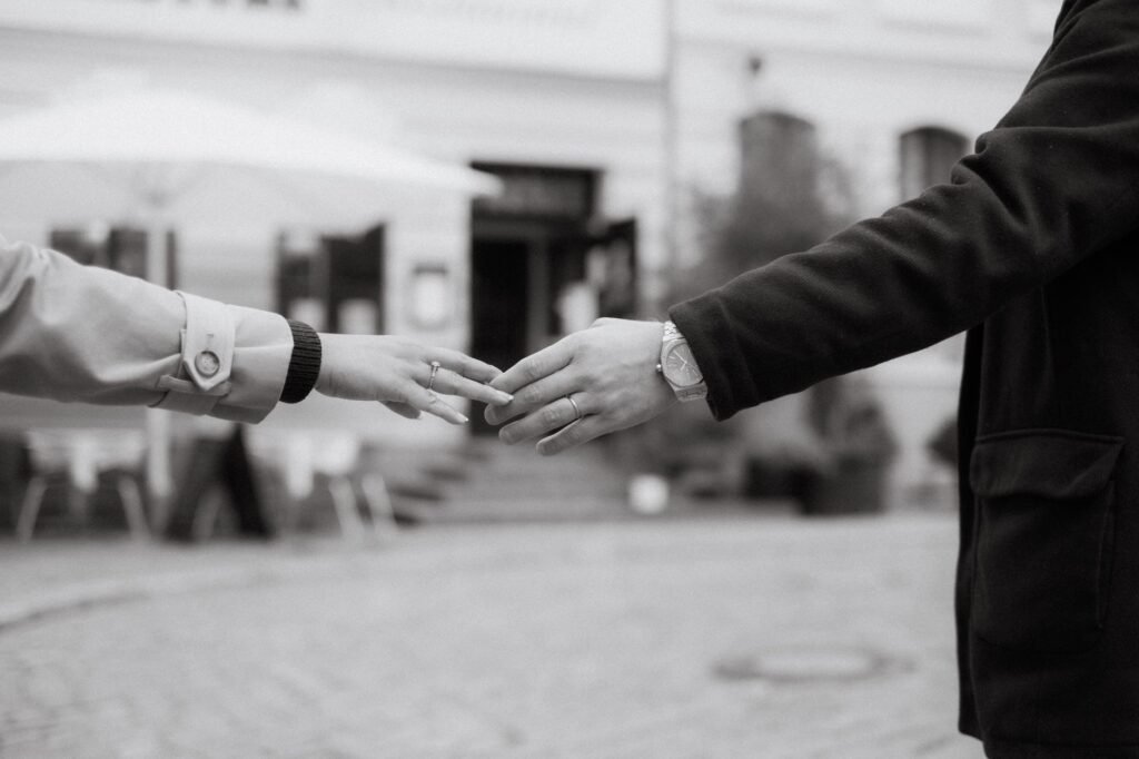 Black and white photo of two people reaching out to hold hands on a city street, symbolizing claddagh ring meaning