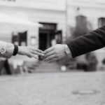 Black and white photo of two people reaching out to hold hands on a city street, symbolizing claddagh ring meaning