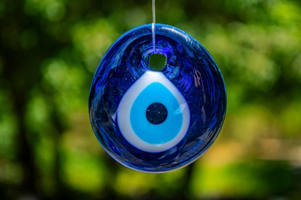 Blue Greek evil eye amulet hanging outdoors against a blurred green background