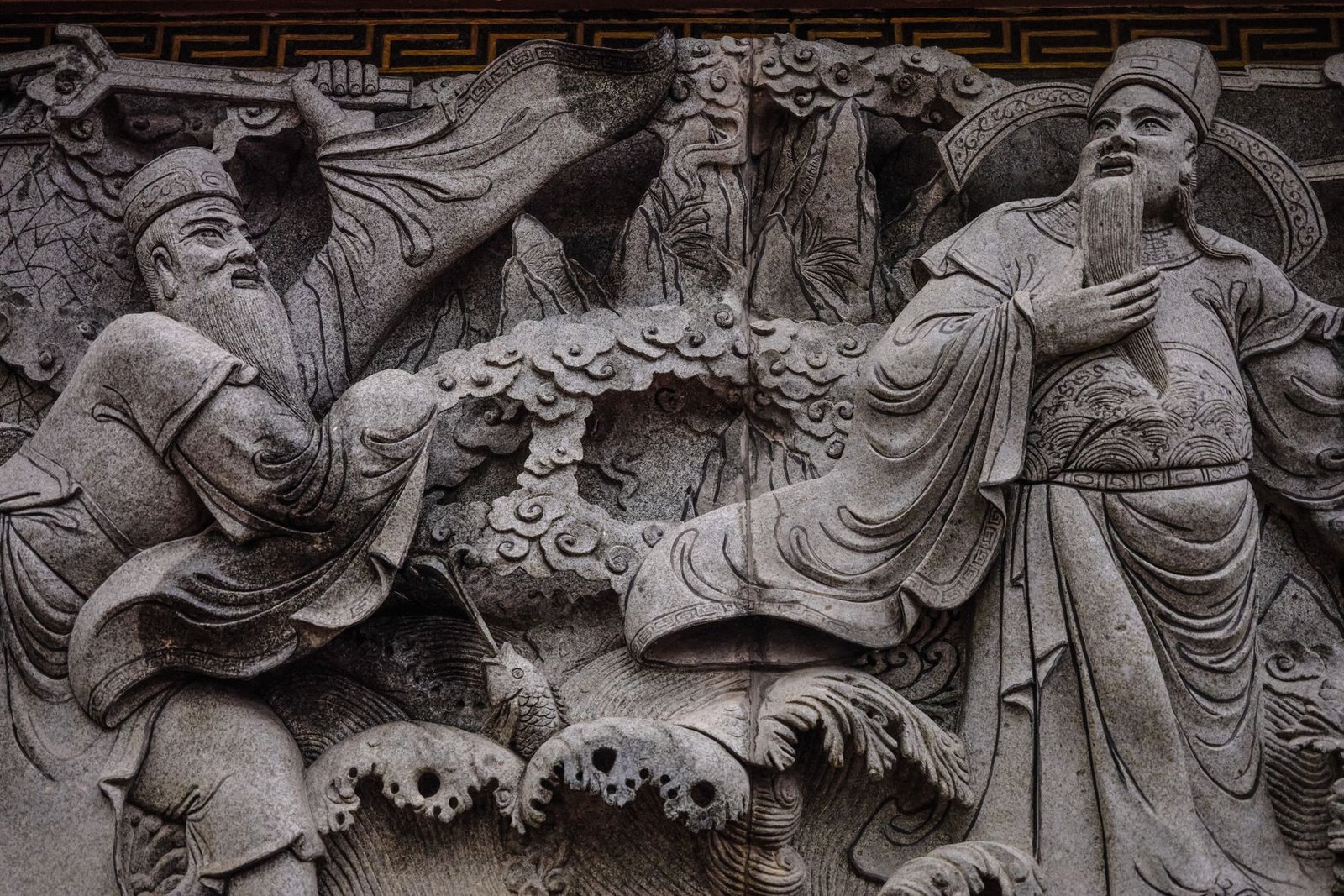 Intricate stone carving of traditional Chinese figures in historical attire, showing Izanagi mythology-inspired imagery