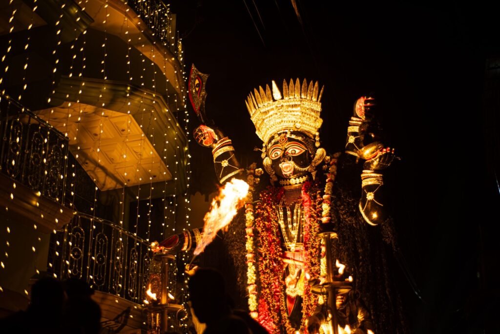 Traditional Indian fire dancer performing with flaming props at a nighttime festival under decorative lights