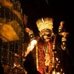 Traditional Indian fire dancer performing with flaming props at a nighttime festival under decorative lights
